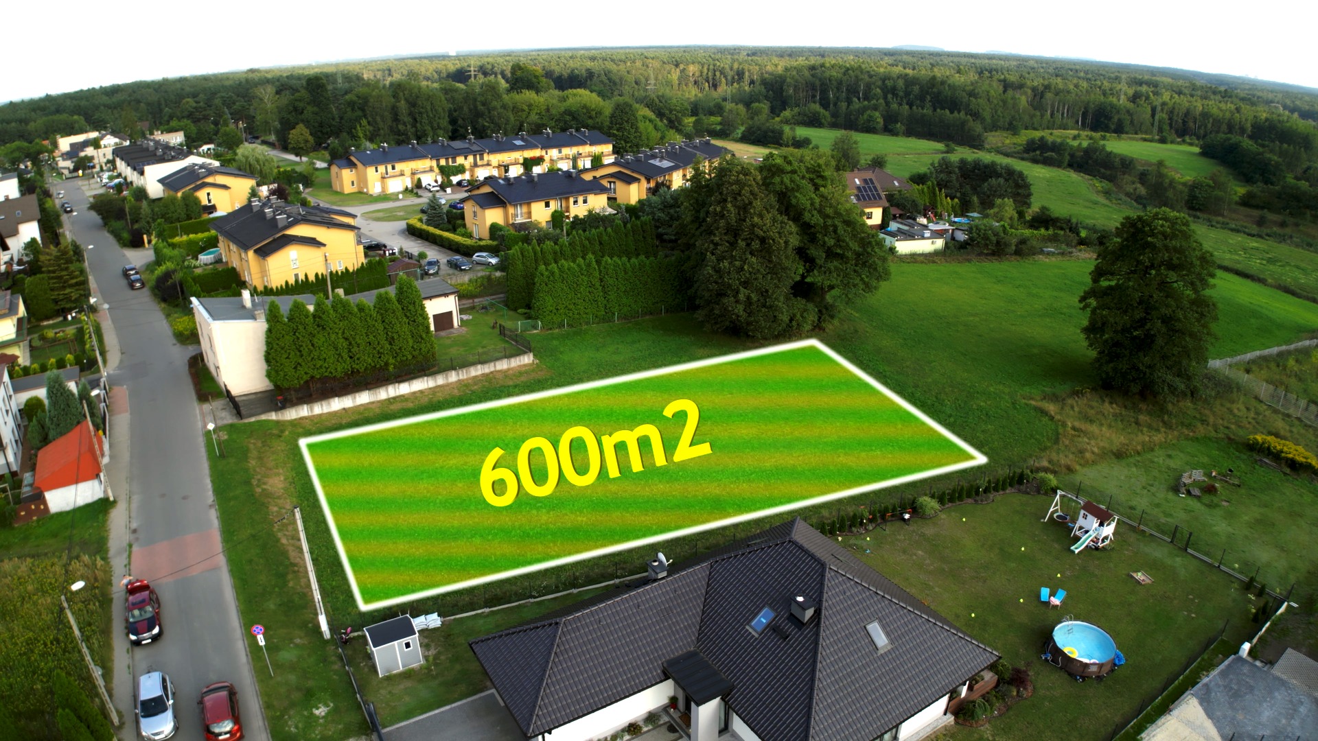 Działka budowlana 600m2 z lotu ptaka, wizualizacja granic na tle domów jednorodzinnych i zieleni.