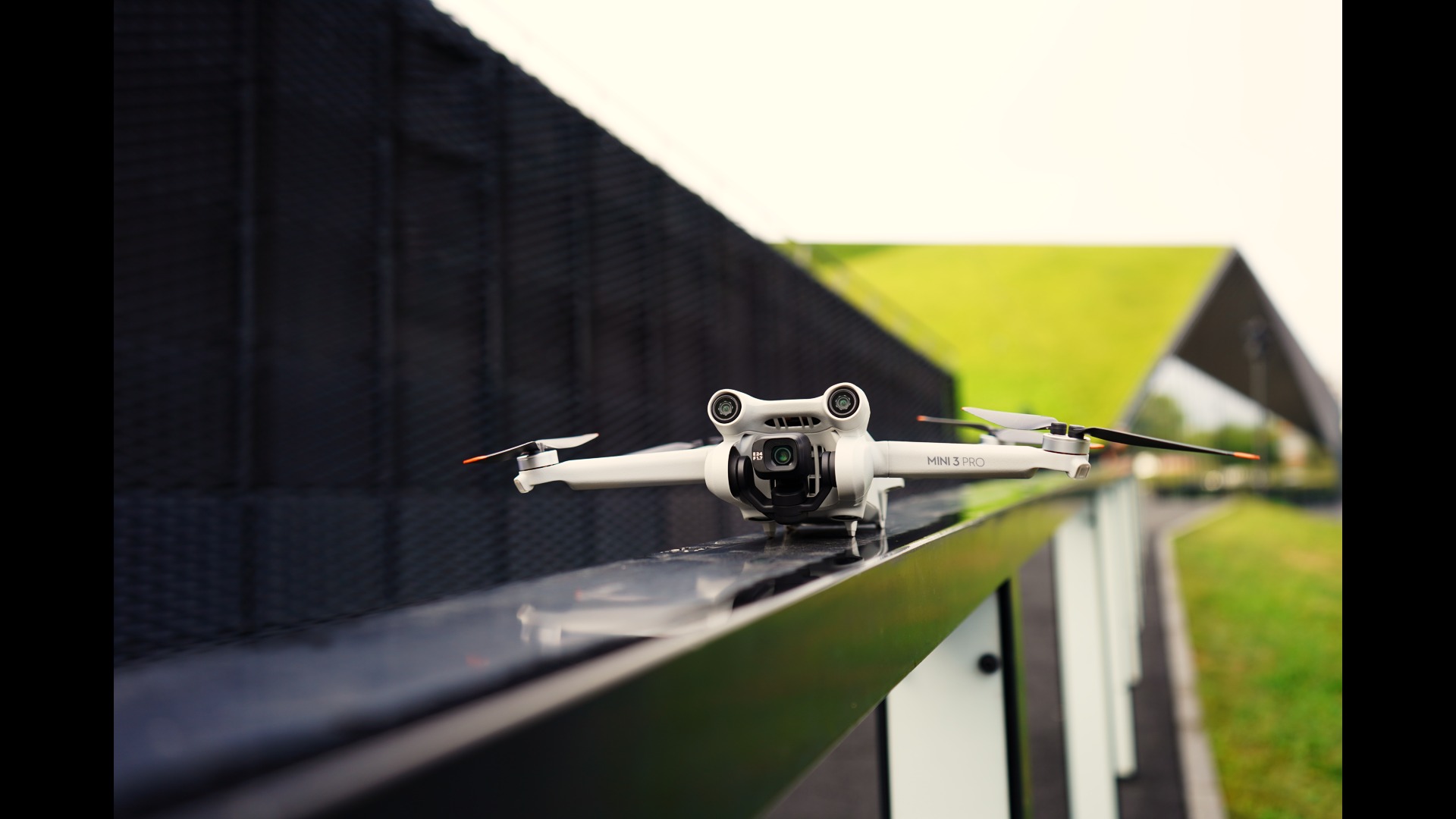 Biały dron DJI Mini 3 Pro na metalowej balustradzie z widokiem na budynek z zielonym dachem