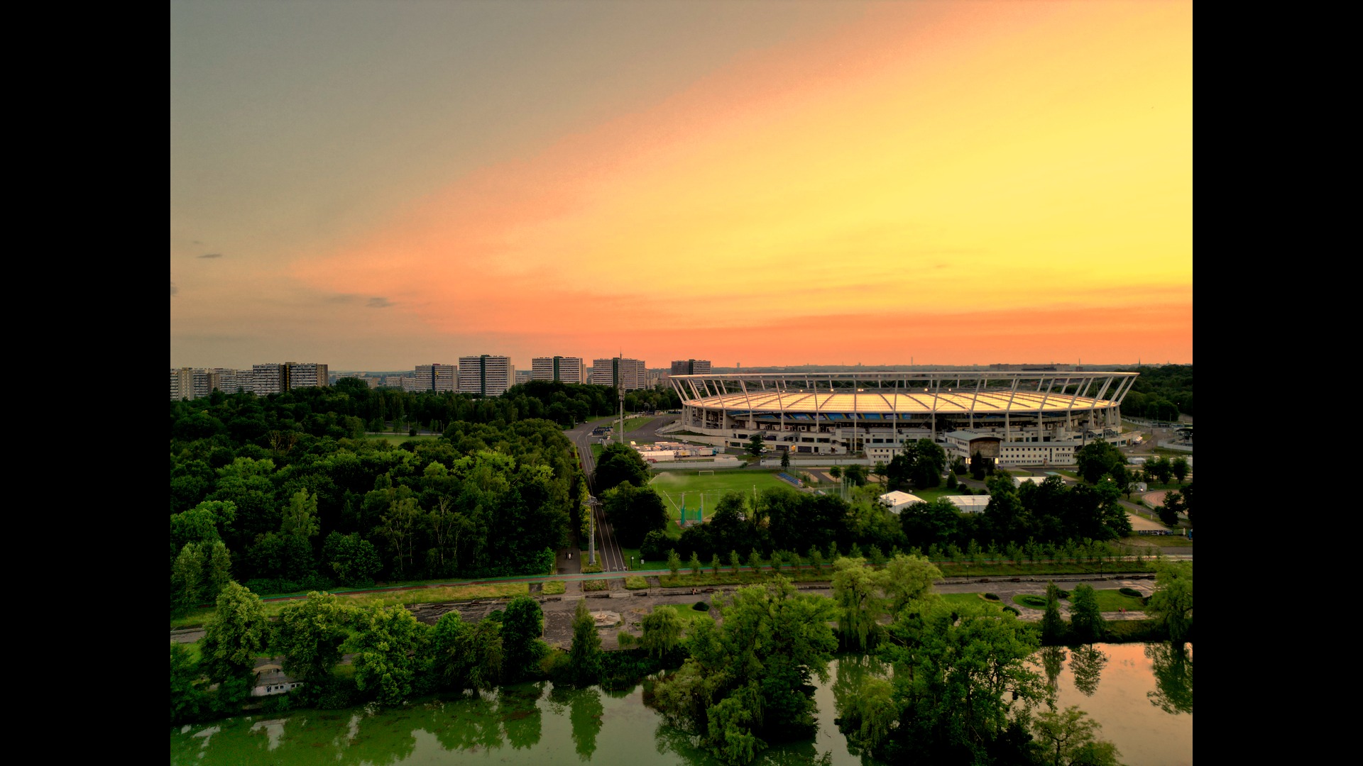 Panorama Ruda Śląska o zmierzchu: stadion miejski otoczony zielenią parkową i budynkami mieszkalnymi, sfotografowany z lotu ptaka przy zachodzącym słońcu.