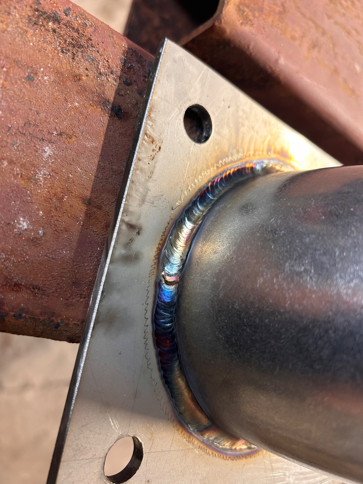 Szlifowany spaw łączący rurę ze stalową płytą, widoczne ślady obróbki i przebarwienia termiczne.