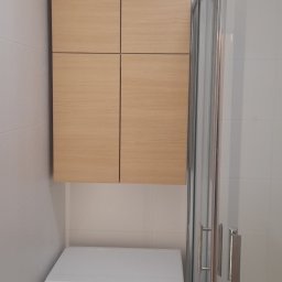 Xeraco Design - Jasna, drewnopodobna szafka wisząca nad białą pralką w łazience z kabiną prysznicową.