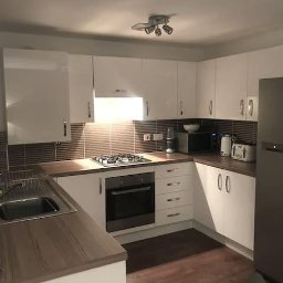 Xeraco Design - Nowoczesna kuchnia z białymi, błyszczącymi szafkami, brązowym blatem i płytkami, srebrną lodówką oraz oświetleniem punktowym.