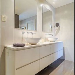 Xeraco Design - Nowoczesna łazienka z podwójną umywalką nablatową, długą szafką z białymi frontami na wysoki połysk i dwoma dużymi lustrami na ścianie wyłożonej jasnymi płytkami.