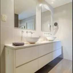 Nowoczesna łazienka z podwójną umywalką nablatową, długą szafką z białymi frontami na wysoki połysk i dwoma dużymi lustrami na ścianie wyłożonej jasnymi płytkami.