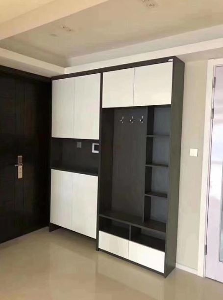 Nowoczesna szafa w przedpokoju z białymi frontami i ciemnoszarym korpusem, zawierająca szafki, półki i wieszaki, umieszczona obok ciemnych drzwi wejściowych.