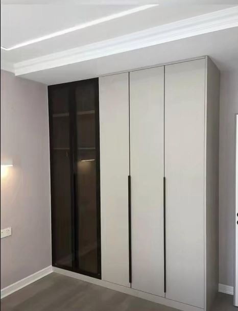 Nowoczesna szafa wnękowa z białymi frontami i czarnymi, długimi uchwytami, z jedną częścią przeszkloną z ciemnego szkła, w jasnym pomieszczeniu z listwą przysufitową.