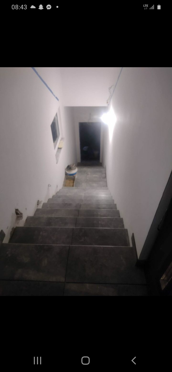 Schody wyłożone ciemnymi płytkami, widok z góry, ściany pomalowane na biało, widoczne ślady po kleju, wiadro z farbą na podeście.