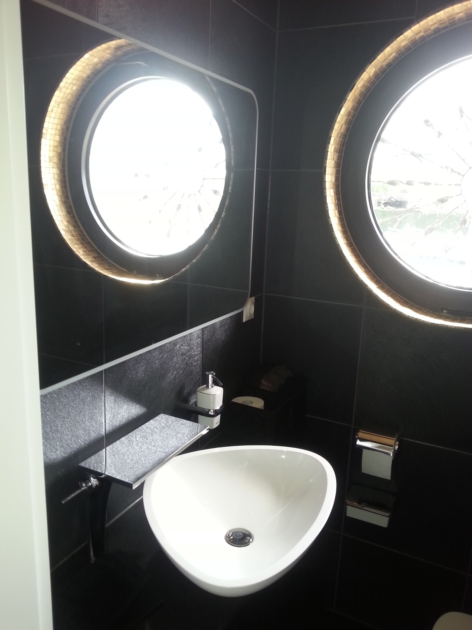 Nowoczesna łazienka w Kowalowej z czarnymi płytkami, okrągłymi oknami z mozaiką, białą umywalką i czarną armaturą.