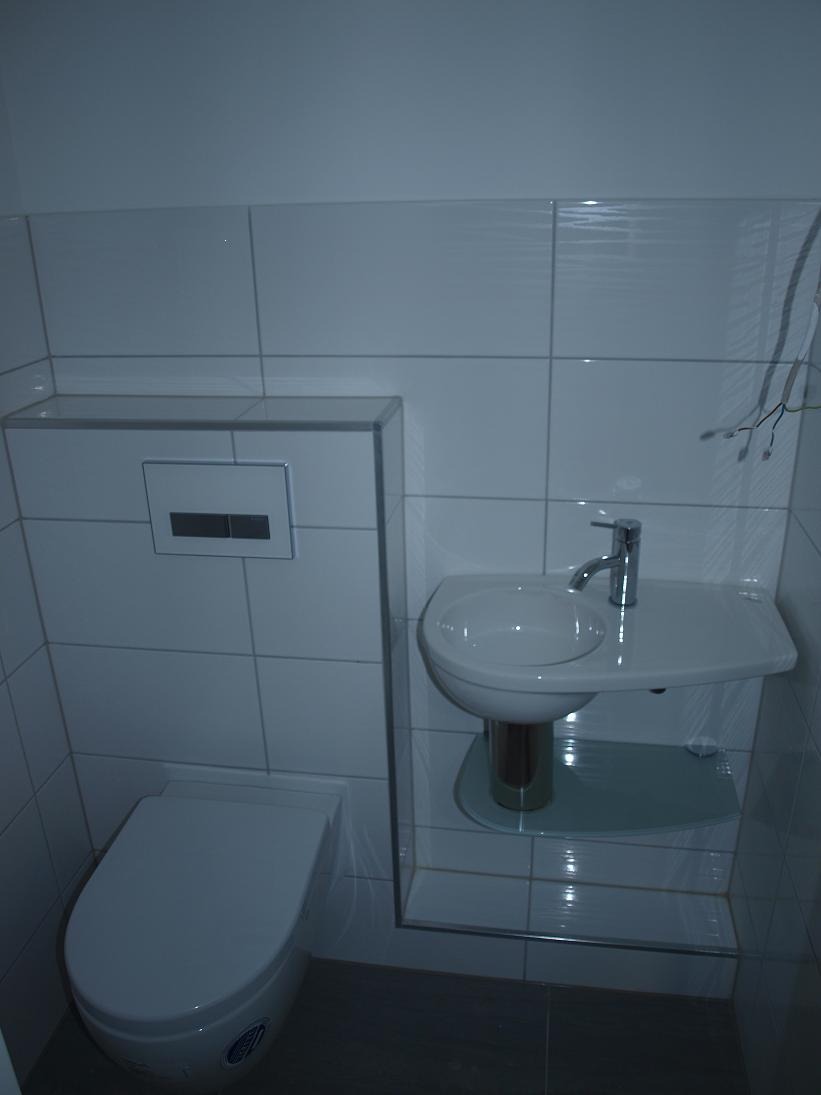 Nowoczesna łazienka z podwieszaną toaletą i umywalką na postumencie, wykończona białymi, kwadratowymi płytkami z delikatną teksturą.