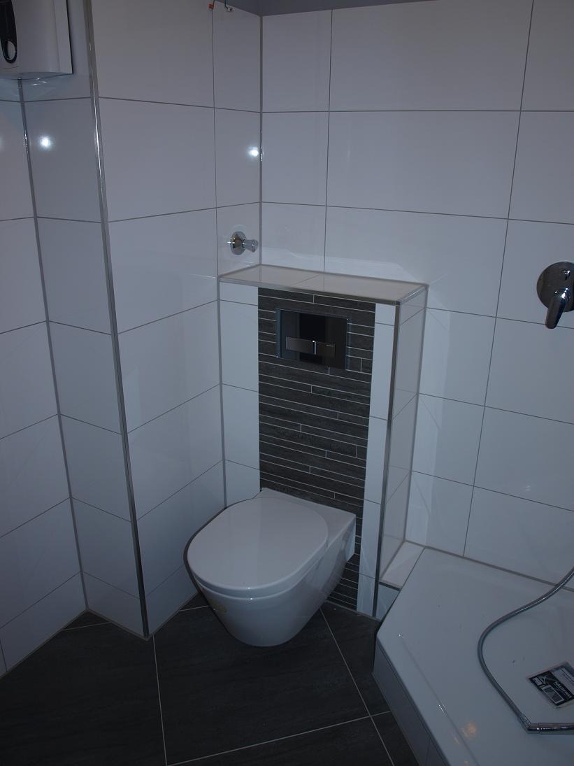 Nowoczesna łazienka z podwieszanym WC, obudowanym szarą mozaiką i białymi płytkami wielkoformatowymi, chromowana armatura.