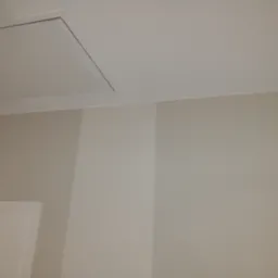 Świeżo pomalowane wnętrze z widocznym włazem na poddasze i czujnikiem ruchu na ścianie, ściany w odcieniach beżu.