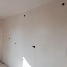 Wnętrze w trakcie szpachlowania ścian z widocznymi otworami na puszki elektryczne i fragmentem podłogi.