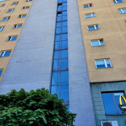 High level - Wysoki budynek z wieloma oknami, z widoczną reklamą na szczycie i klimatyzacją na dole, sfotografowany z dołu.