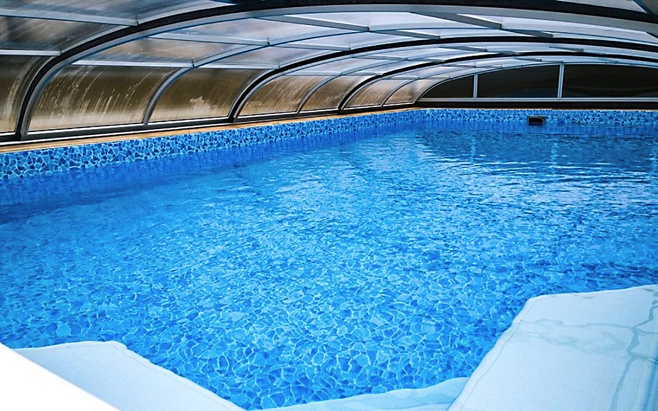 Kryty basen z mozaiką, widok na błękitną wodę i zadaszenie z przezroczystych paneli.