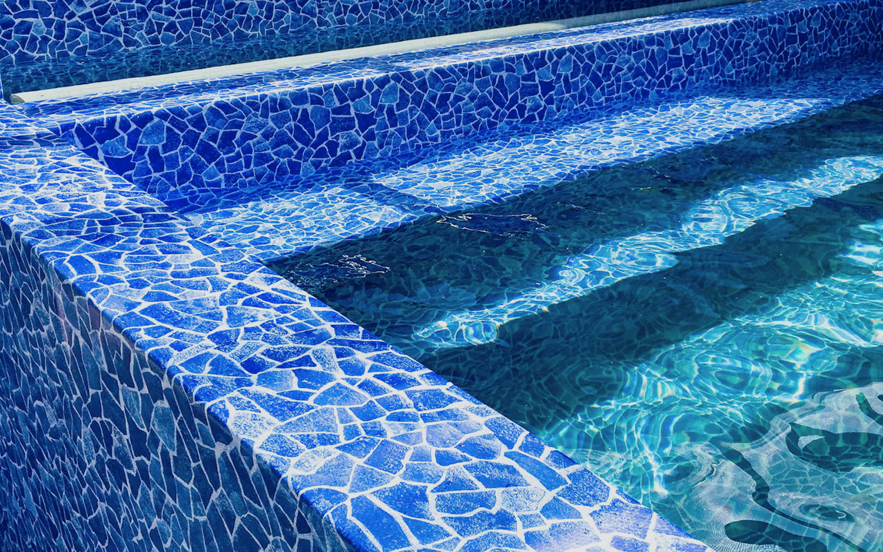 Błękitna mozaika wykończenia schodów w basenie, woda odbija światło tworząc falujące wzory.