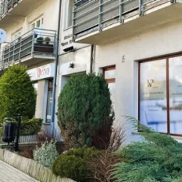 Fasada budynku w Pabianicach z widocznym oknem biura rachunkowego KP Support oferującego usługi księgowe i kadrowe, przysłonięta częściowo przez krzewy.