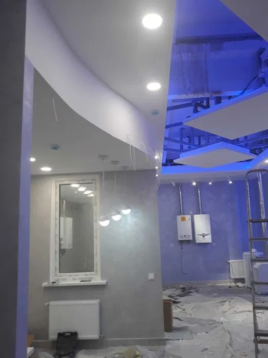 Wnętrze w trakcie prac wykończeniowych: gładkie ściany, częściowo zamontowany sufit podwieszany z oświetleniem punktowym i dekoracyjnym niebieskim podświetleniem, zabezpieczona podłoga, grzejnik...