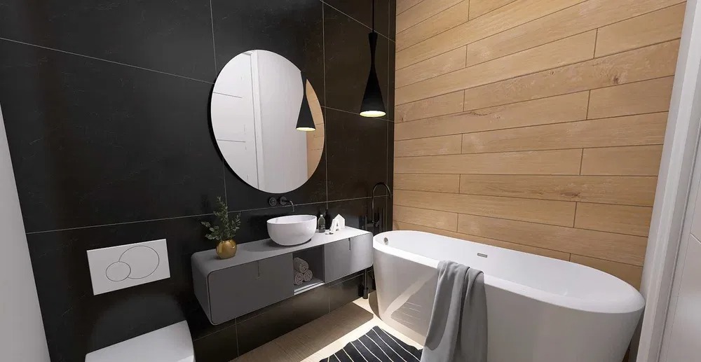 Nowoczesna łazienka z czarnymi płytkami, drewnopodobną okładziną, okrągłym lustrem, wiszącą szafką z umywalką i wolnostojącą wanną z szarym ręcznikiem.