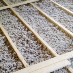 U R.B - Izolacja poddasza wełną mineralną, widoczne drewniane legary. Etap prac przed zakryciem izolacji. Ujęcie z góry, oświetlenie naturalne.