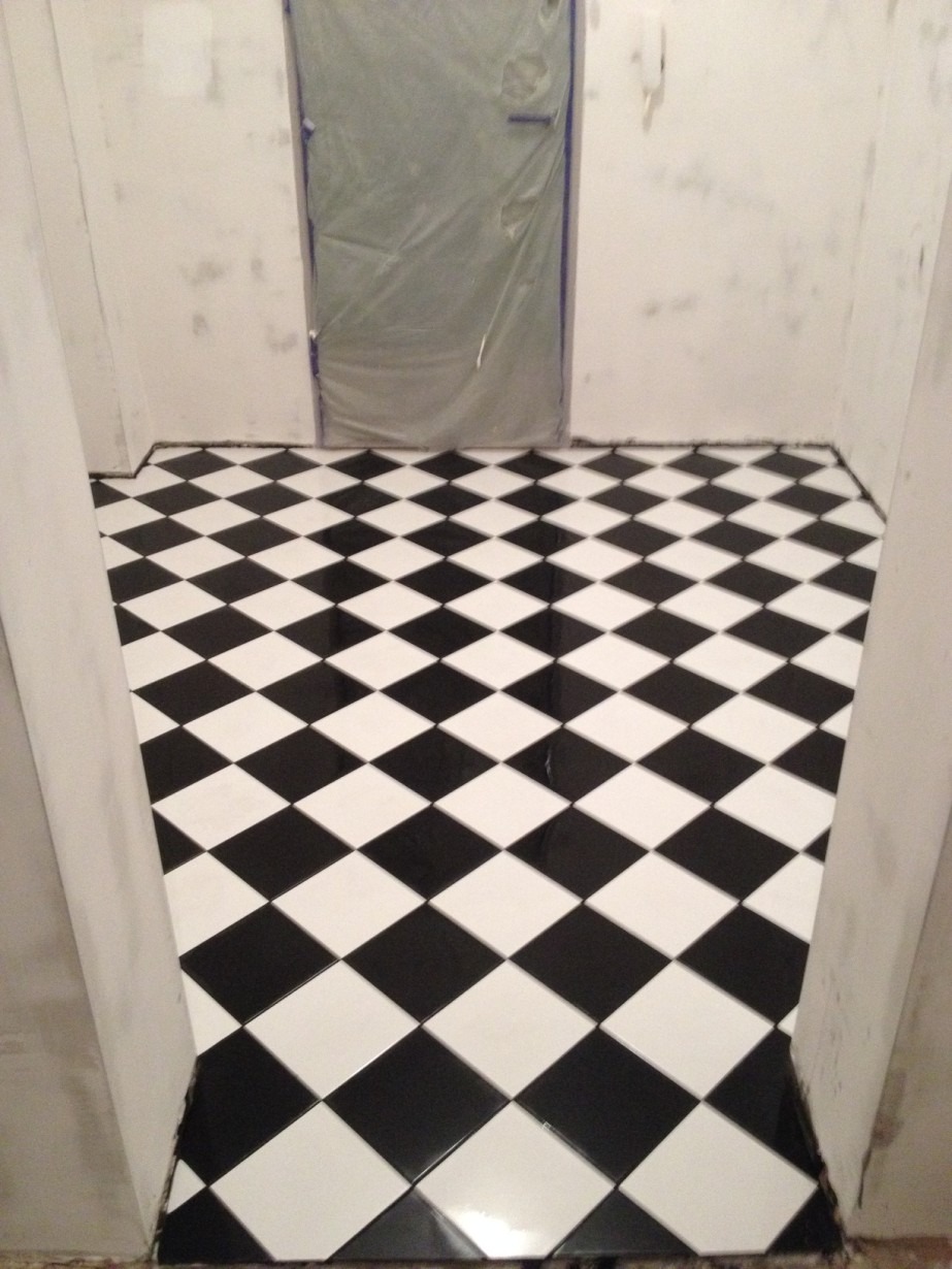 Ułożona czarno-biała podłoga z płytek w romby w trakcie prac wykończeniowych, zabezpieczone drzwi folią malarską.