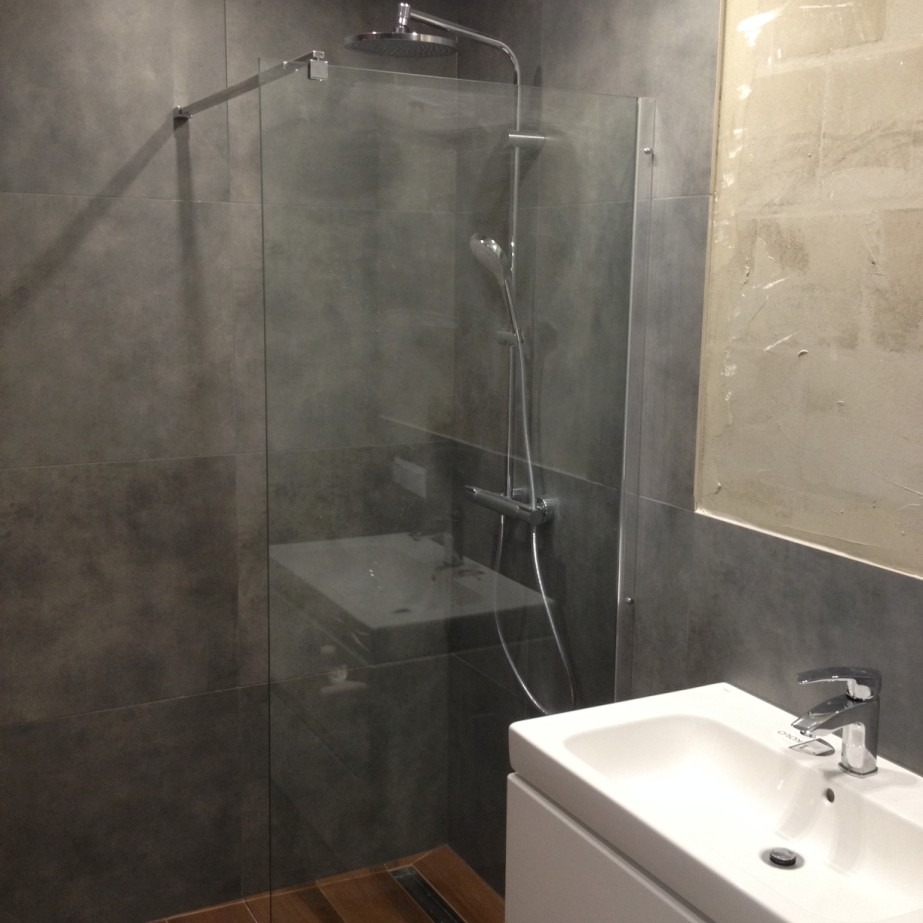 Szara łazienka z kabiną prysznicową typu walk-in, białą umywalką i fragmentem ściany przygotowanej do malowania.