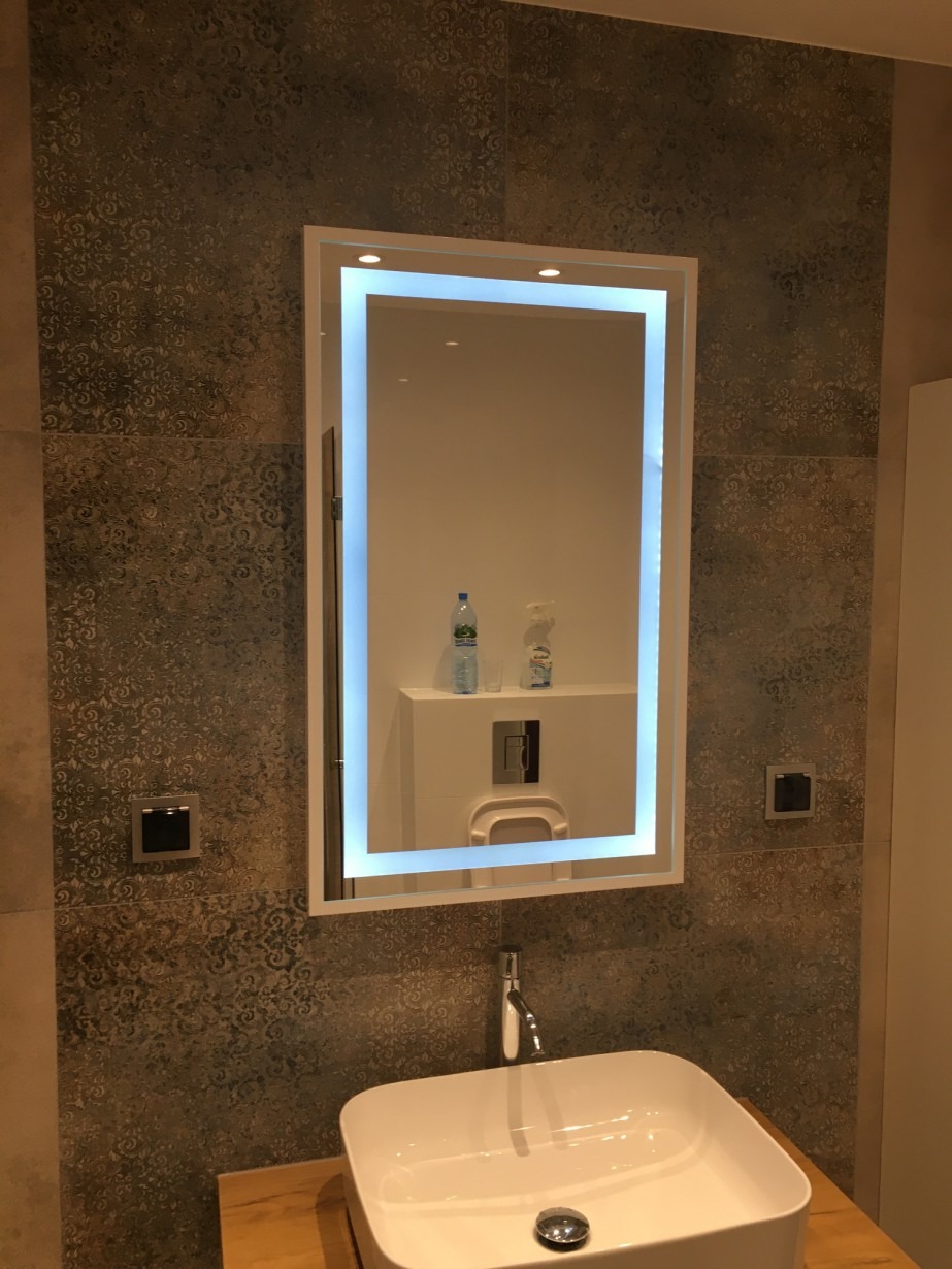 Nowoczesna łazienka z umywalką nablatową, podświetlanym lustrem LED i dekoracyjnymi płytkami w odcieniach brązu i szarości.