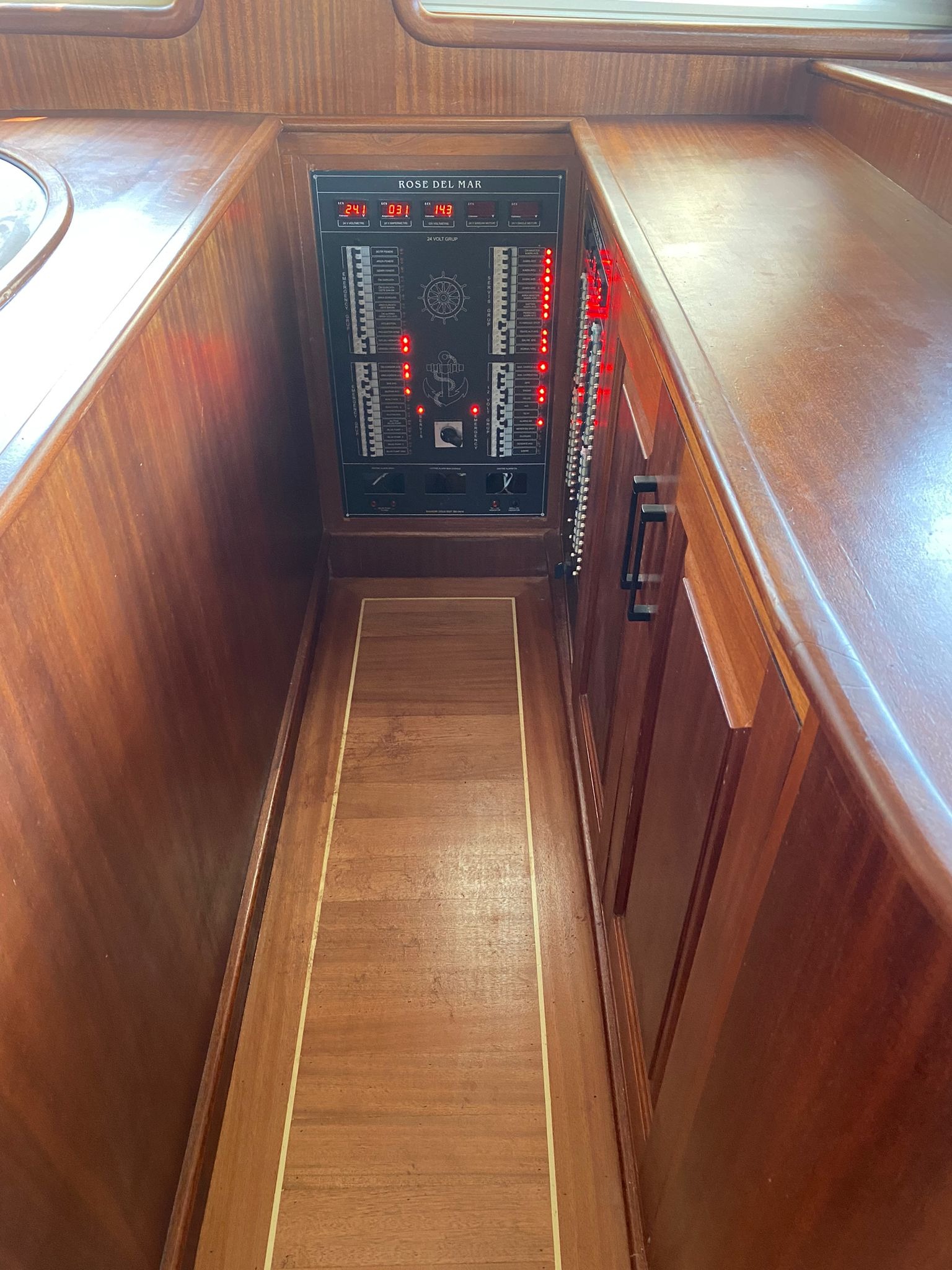 Wnętrze jachtu z drewnianą zabudową, widoczny panel sterowania z wyświetlaczami i wskaźnikami, oświetlony czerwonymi diodami.