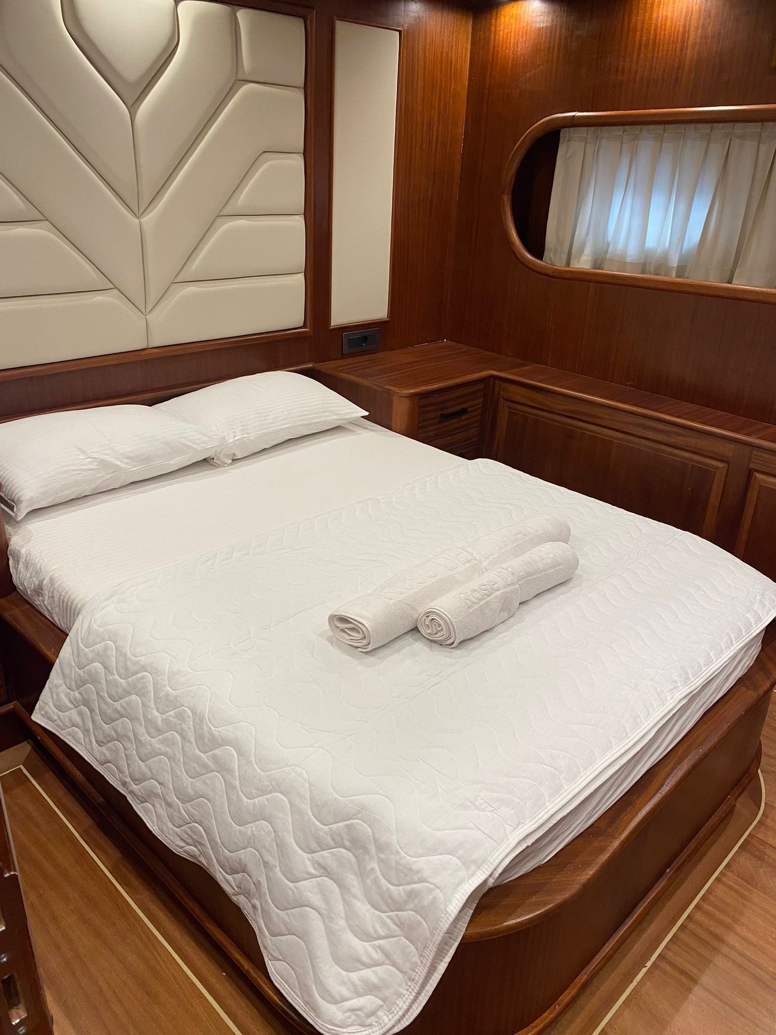 Kabinowa sypialnia na jachcie z drewnianymi panelami, łóżkiem z białą pościelą i dwoma zwiniętymi ręcznikami.