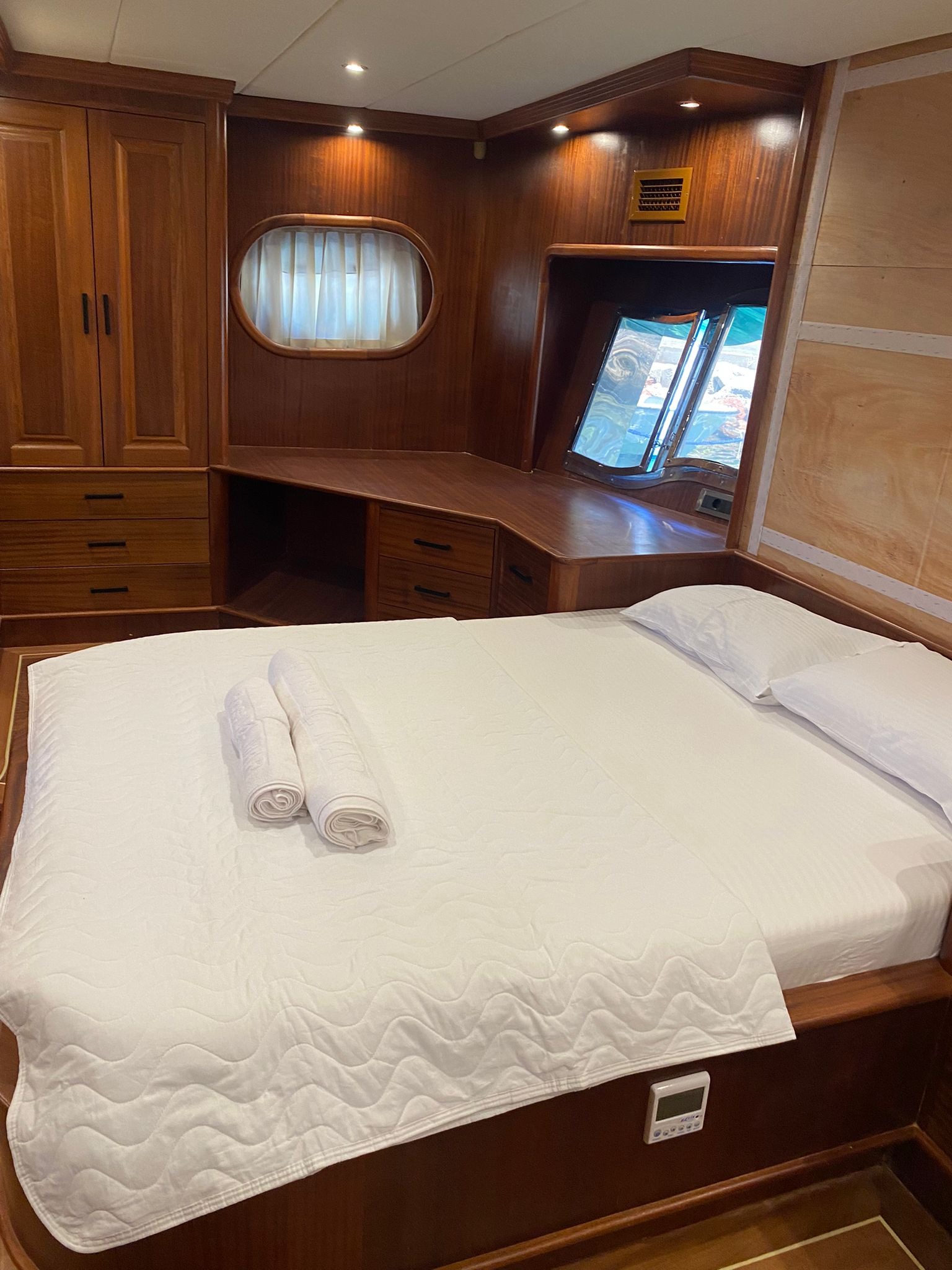 Kabinowe wnętrze jachtu z drewnianą zabudową, łóżkiem z białą pościelą i oknem z widokiem na wodę.
