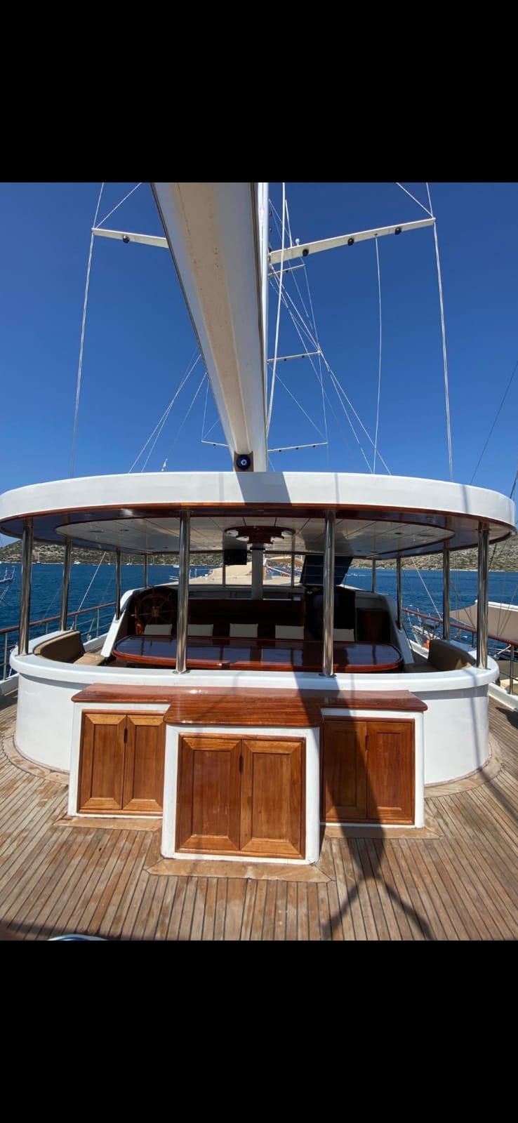 Pokład luksusowego jachtu żaglowego z drewnianą podłogą, kabinami z mahoniowymi drzwiami i zadaszeniem z widokiem na morze i błękitne niebo.