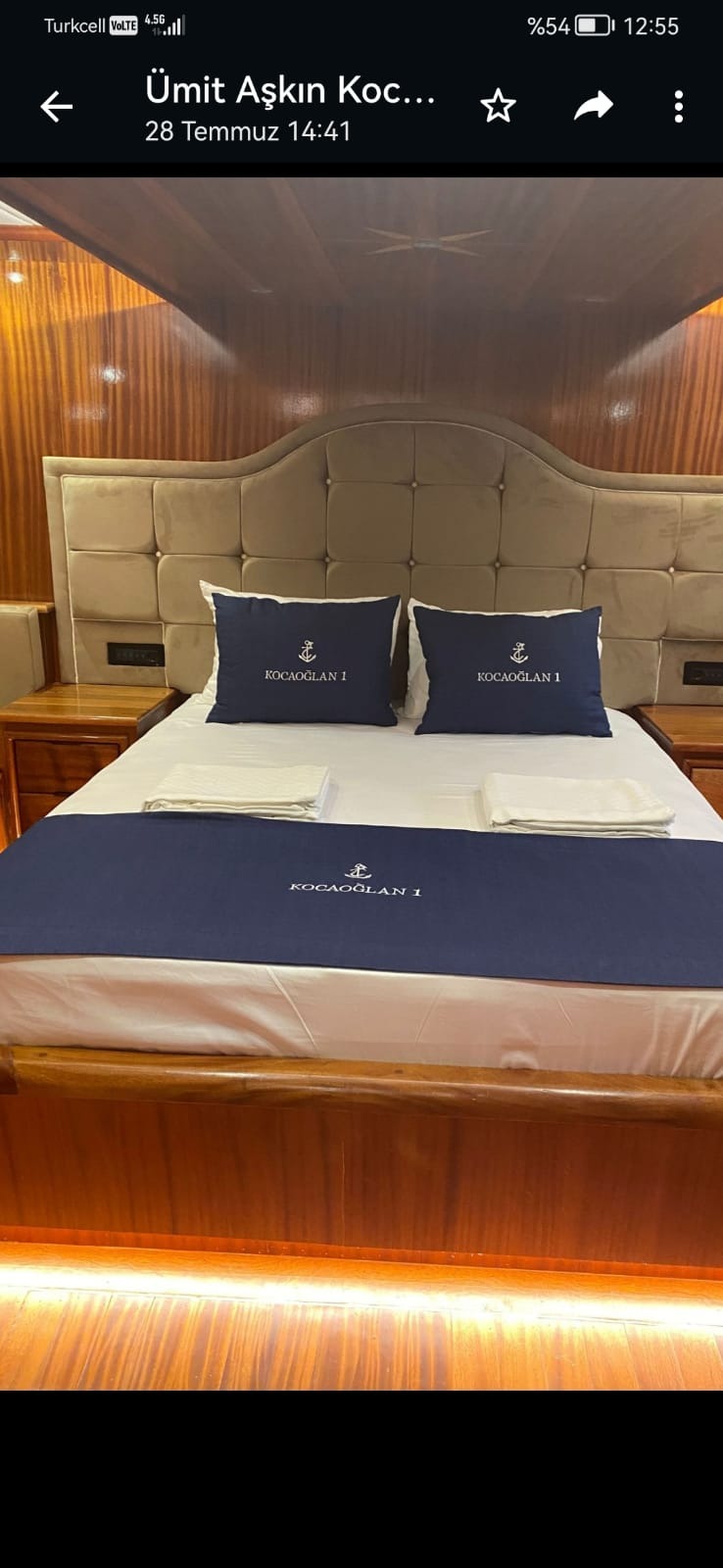Wnętrze kabiny jachtu z łóżkiem z ciemnego drewna, poduszki i narzuta z logo Kocaoğlan 1.