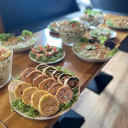 Stół z różnorodnymi potrawami: sałatki w szklanych misach, roladki z szynką i warzywami na białym talerzu, dekorowane zieleniną.