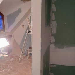 Eryk Jabłoński wykończenia dekarstwo brukarstwo i gwarancja - Pokój w trakcie remontu: widoczna ściana z zielonej płyty karton gips, łączenia szpachlowane, w tle drabina i lampa budowlana.