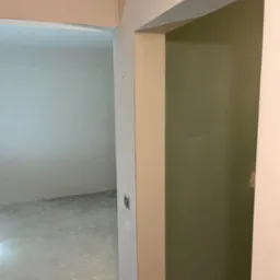 Wnętrze w trakcie prac wykończeniowych, widoczne ściany w dw&oacute;ch odcieniach (jasny szary i oliwkowy), surowy beton na podłodze oraz otw&oacute;r drzwiowy z widocznymi niedoskonałościami na ościeżnicy.