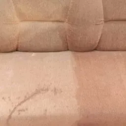 Częściowo wyczyszczona, beżowa kanapa z widocznym zabrudzeniem po lewej stronie i efektem czyszczenia po prawej.