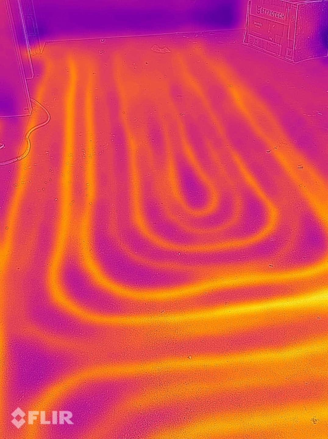 Termowizja ułożonej instalacji ogrzewania podłogowego, widoczne rury w kształcie spirali, pomarańczowo-fioletowa kolorystyka, karton Styrotech w tle.