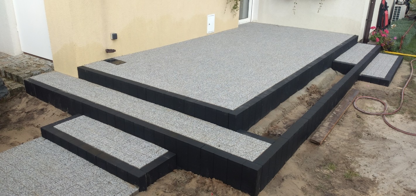 Granitowe schody z czarnymi obrzeżami prowadzące na taras, widoczne ślady prac ziemnych.