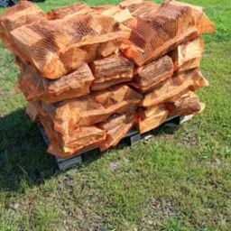 Stos worków z drewnem kominkowym ułożonych na drewnianej palecie, widoczne na tle zielonej trawy.