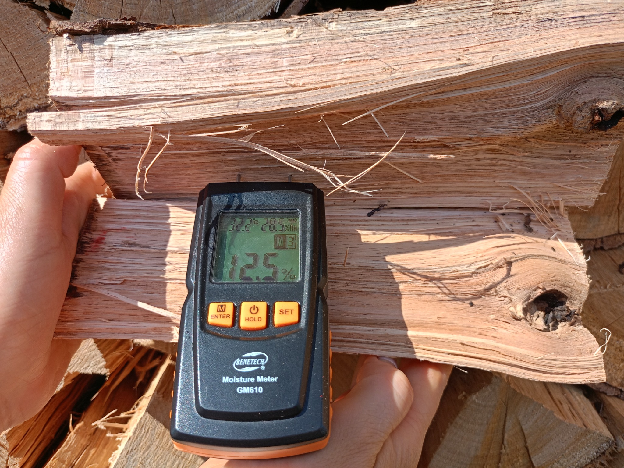 Pomiar wilgotności rozszczepionego kawałka drewna kominkowego za pomocą wilgotnościomierza Benetech GM610, wskazującego 12.5% wilgotności.