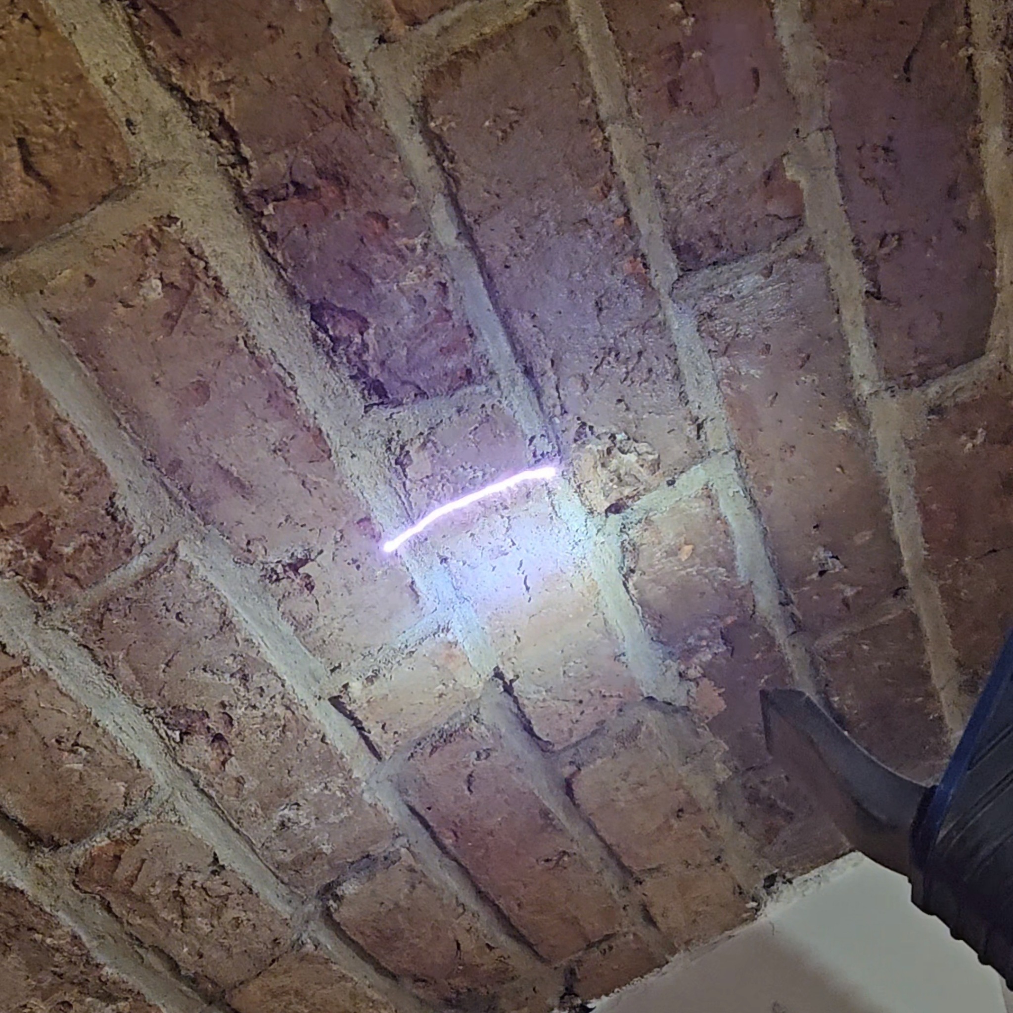 Ceglany sufit z widocznym laserem czyszczącym spoiny, element narzędzia w prawym dolnym rogu kadru.