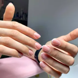 Dłonie z delikatnym, klasycznym manicure francuskim na krótkich, owalnych paznokciach; widoczny lekki połysk lakieru.