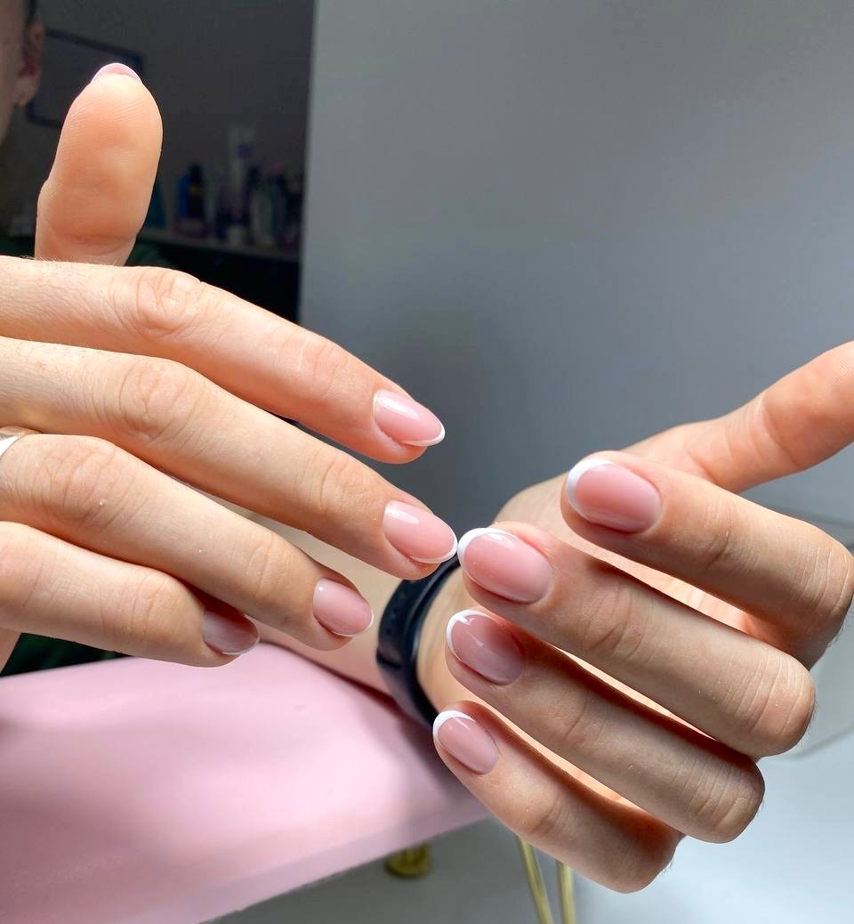 Dłonie z delikatnym, klasycznym manicure francuskim na krótkich, owalnych paznokciach; widoczny lekki połysk lakieru.