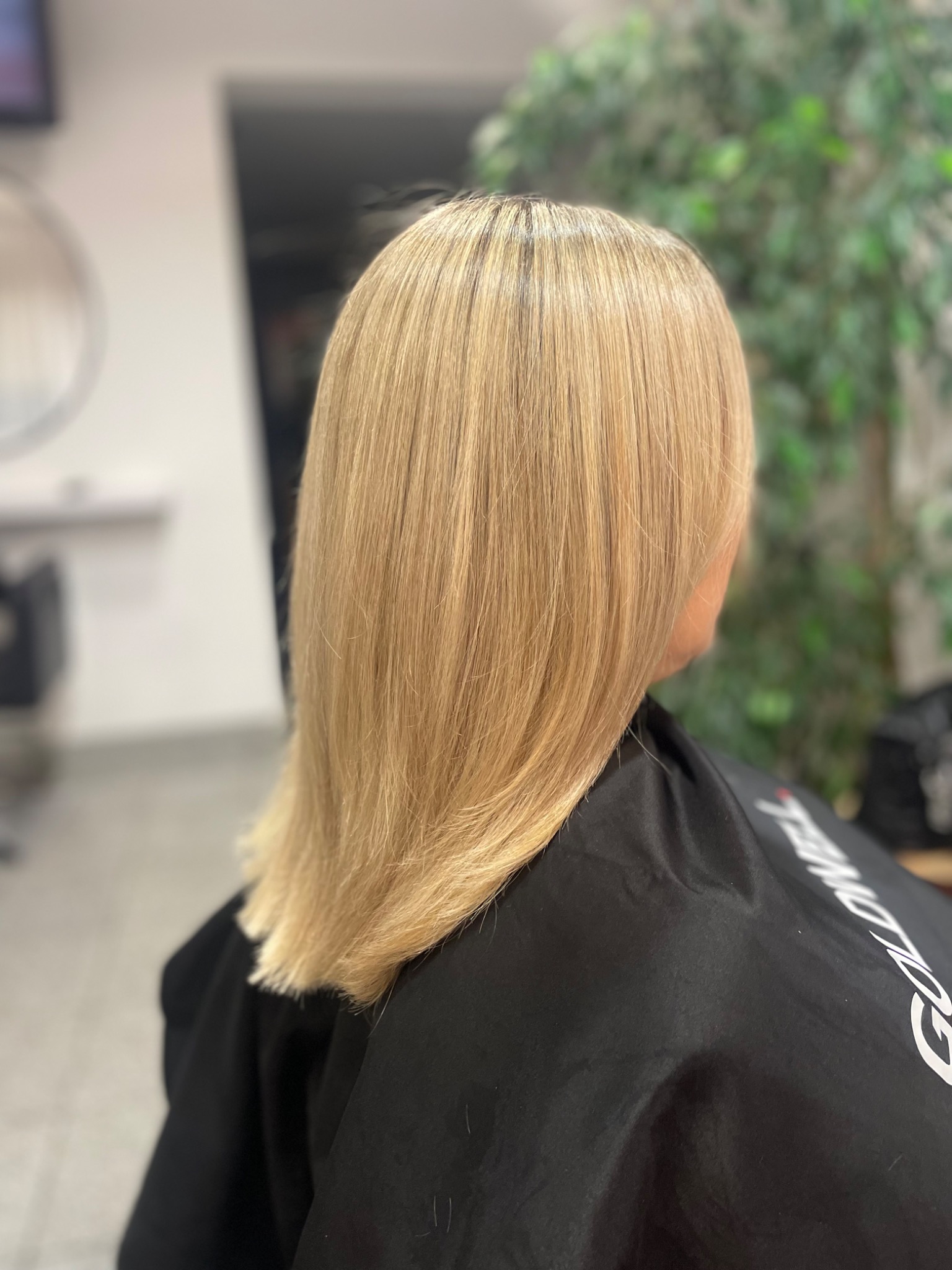 Krótkie, proste blond włosy po koloryzacji, widoczne od tyłu, okryte czarną peleryną w salonie.
