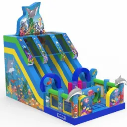 Duży dmuchany zamek ze zjeżdżalniami, motyw oceaniczny z delfinami, rekinami i kolorowymi rybami, widok z perspektywy.