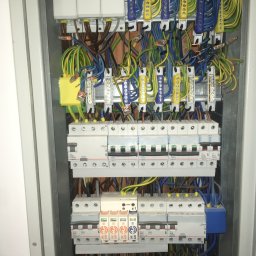 JD Elektroinstalacje - Otwarta skrzynka rozdzielcza z widocznymi bezpiecznikami, przewodami w różnych kolorach i listwami zaciskowymi, ułożonymi w metalowej obudowie.