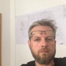 Portret inżyniera z okularami na czole, z planem elektrycznym w tle na ścianie.