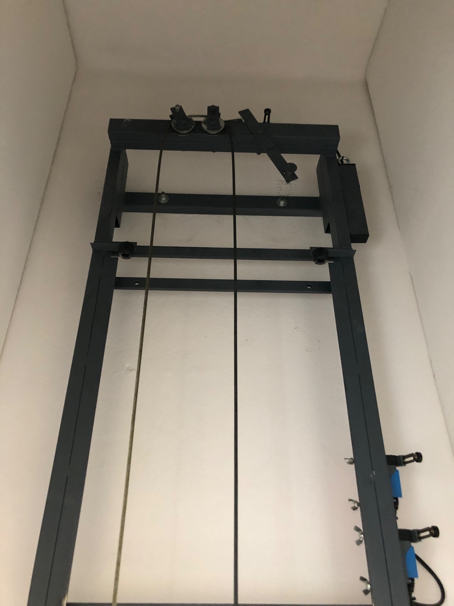 Wnętrze szybu z zamontowaną konstrukcją metalową, prawdopodobnie prowadnicą windy lub innego urządzenia podnoszącego, widoczne liny i elementy mocujące.