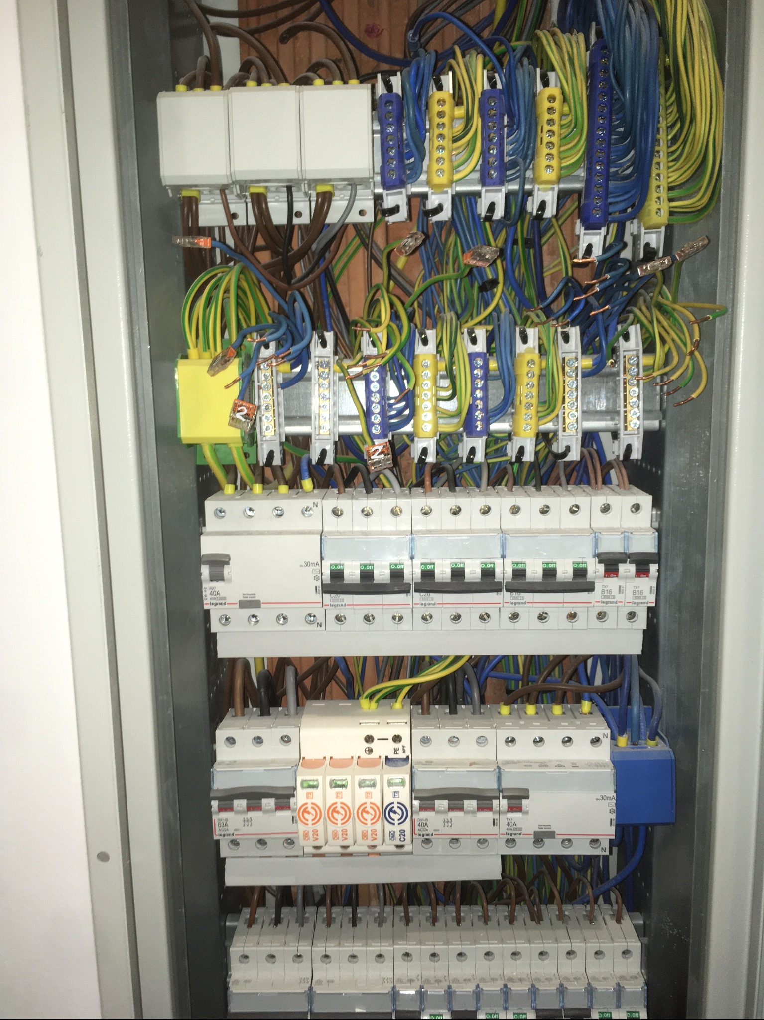 Otwarta skrzynka rozdzielcza z widocznymi bezpiecznikami, przewodami w różnych kolorach i listwami zaciskowymi, ułożonymi w metalowej obudowie.