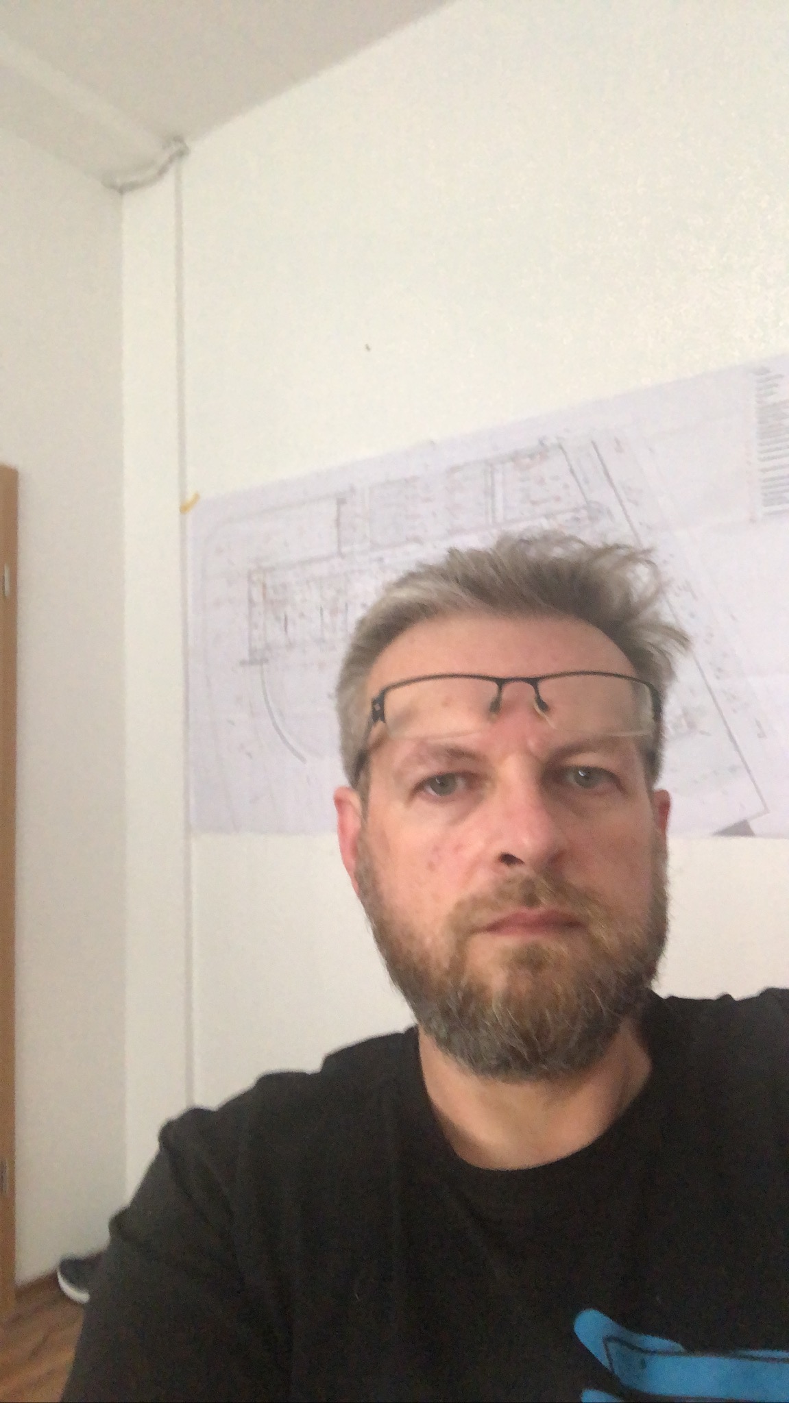 Portret inżyniera z okularami na czole, z planem elektrycznym w tle na ścianie.