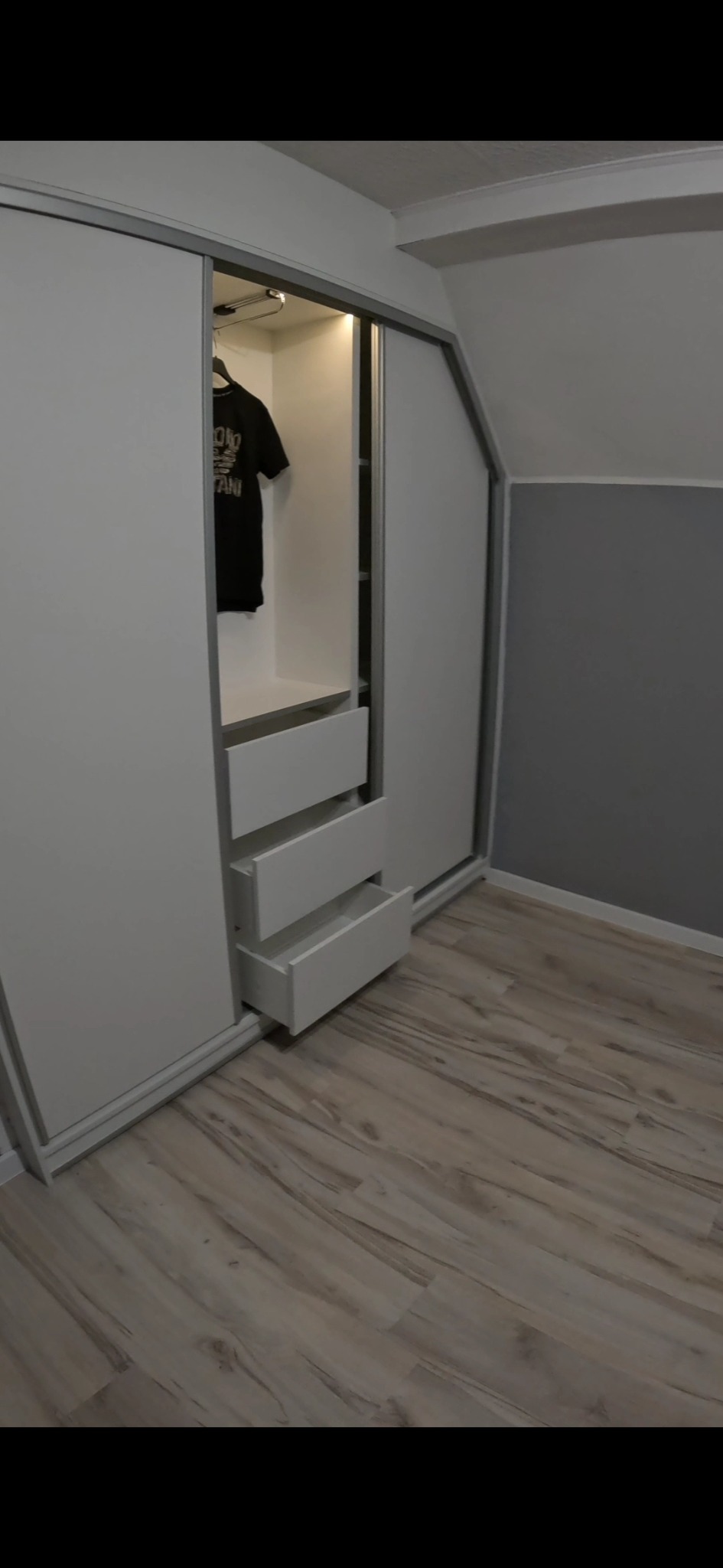 Biała szafa przesuwna z otwartymi szufladami w skosnym pomieszczeniu, widoczne wnętrze szafy z wiszącą koszulką.